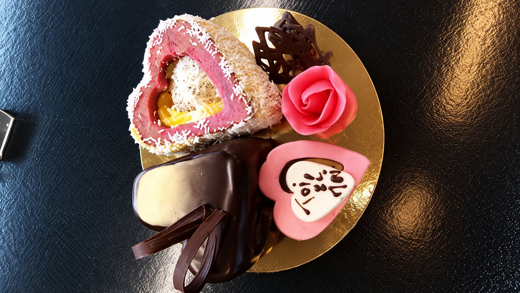 Vue du dessus d'un petit plateau doré garni de chocolats et pâtisseries roses en forme de cœur, d'une rose en massepain et de chocolats noirs.