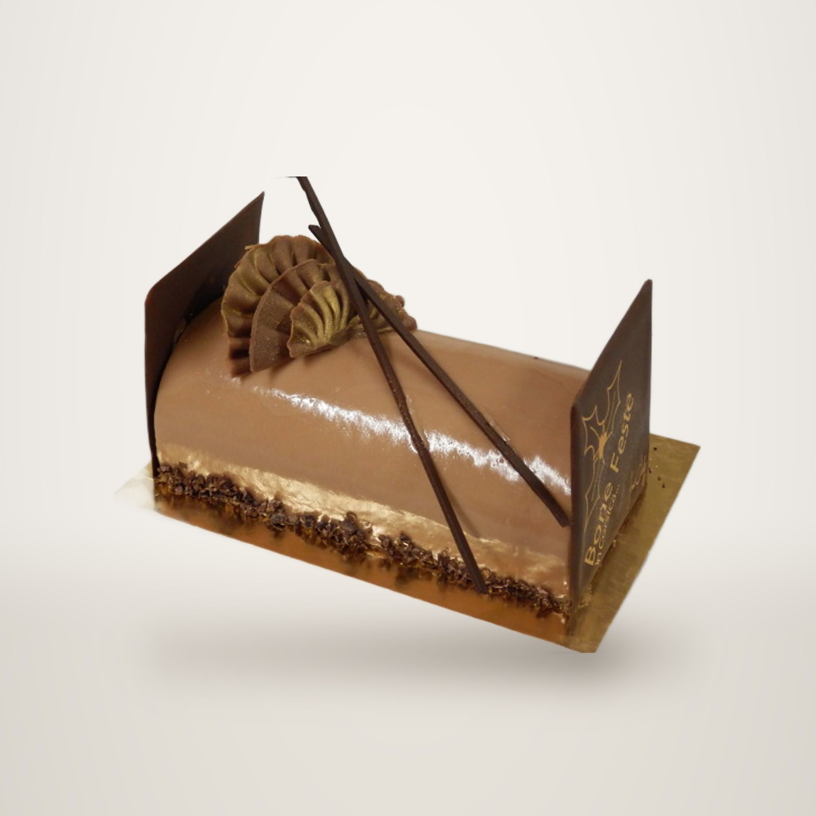 Une bûche de Noël au chocolat au glaçage brillant, ornée de plaques et de bâtonnets en chocolat, posée sur un carton doré.