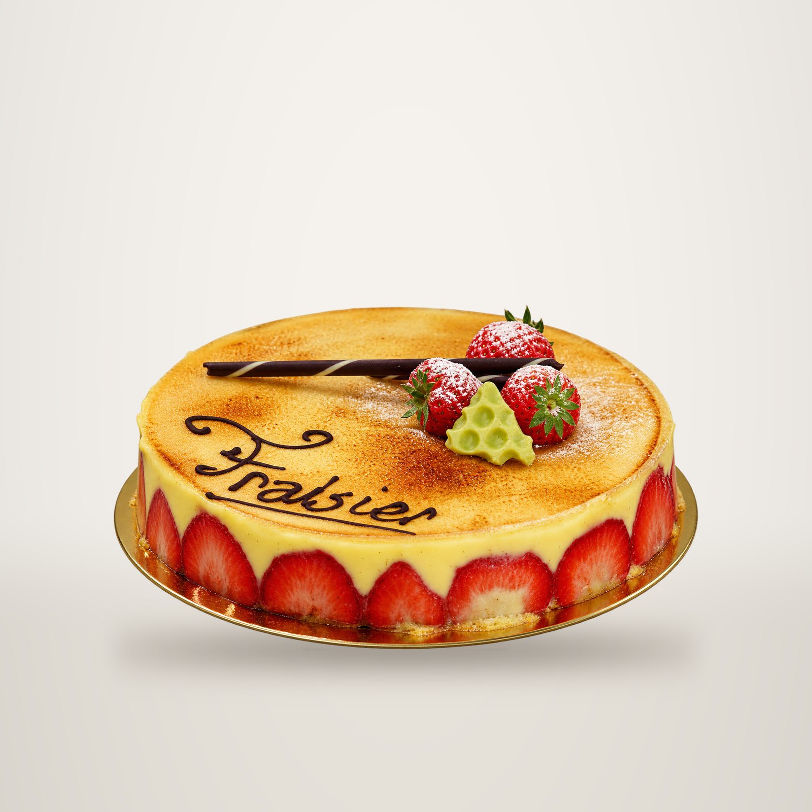 Un gâteau fraisier à la crème jaune pâle, orné de fraises, d'un morceau de chocolat noir et du mot Fraisier écrit en chocolat.