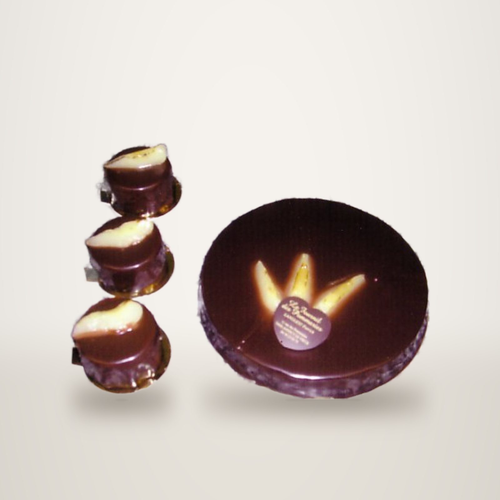 Un grand gâteau rond glacé au chocolat décoré de tranches de poire, posé à côté de trois petits entremets individuels sur un plan de travail en granit.