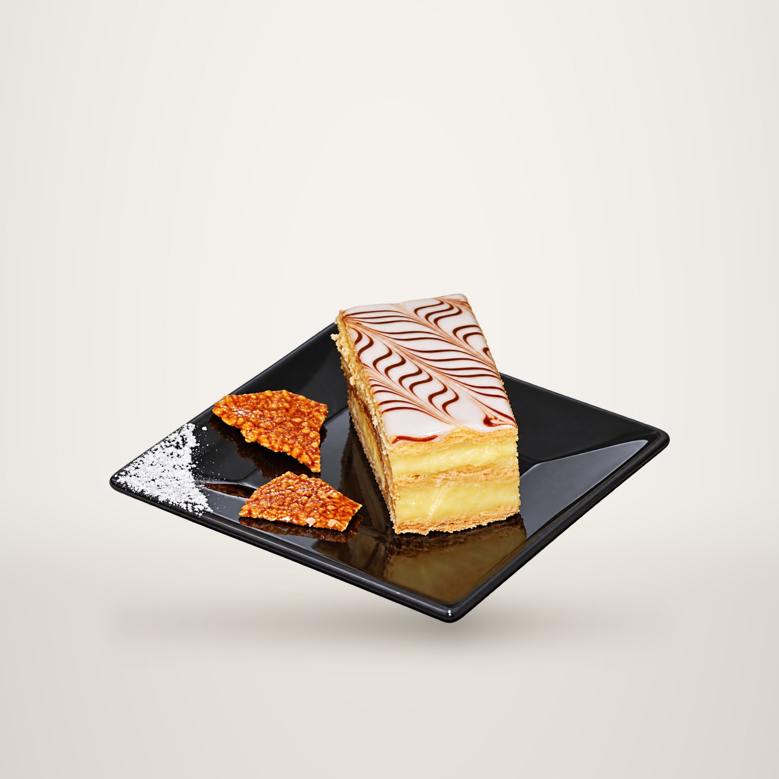 Une part de mille-feuille glacée de motifs chocolatés, servie sur une assiette carrée noire avec deux éclats de caramel aux amandes.