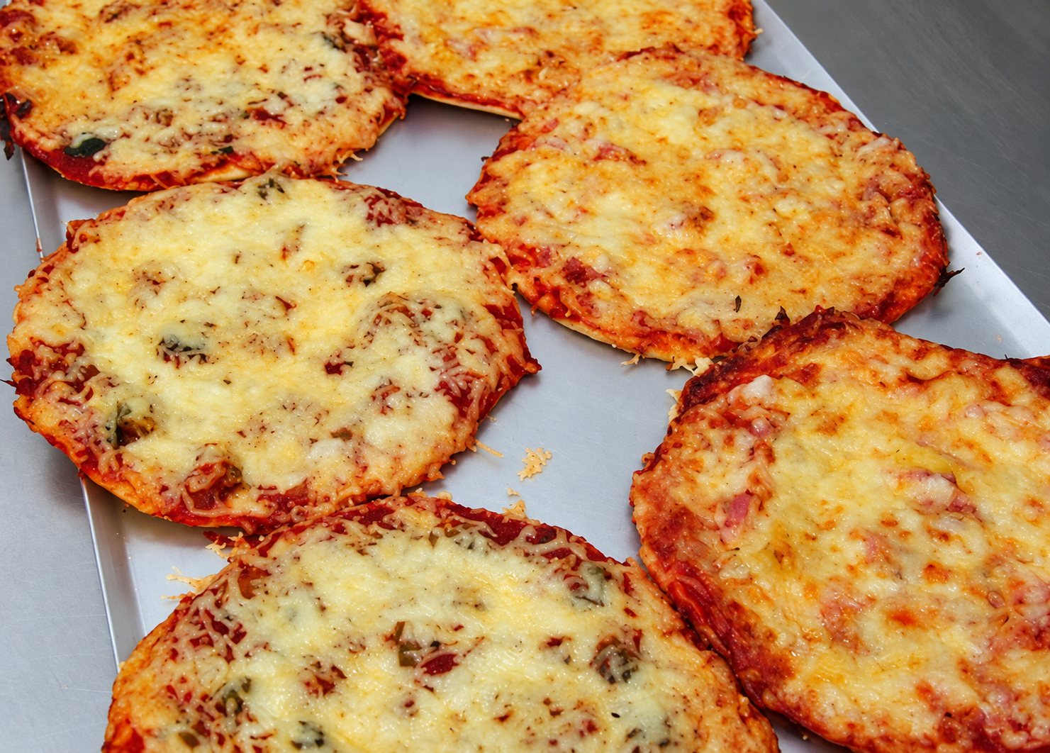 Plusieurs petites pizzas rondes au fromage fondu et doré posées sur une plaque de cuisson métallique.