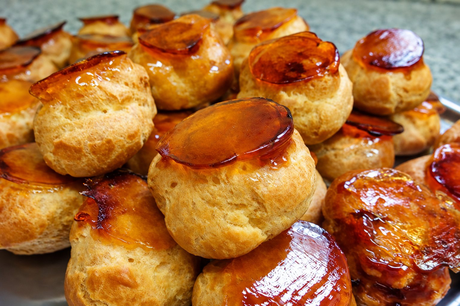Des petits choux à la pâte dorée, glacés d'un caramel brillant, sont empilés sur un plat métallique.